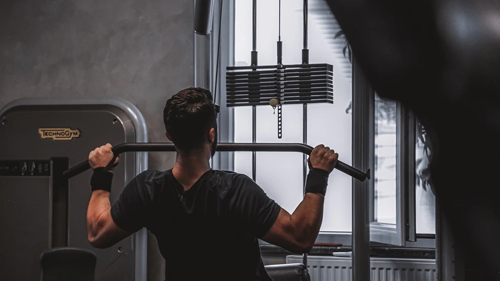 Person tränar med vikter i gym med industriell inredning och stora fönster