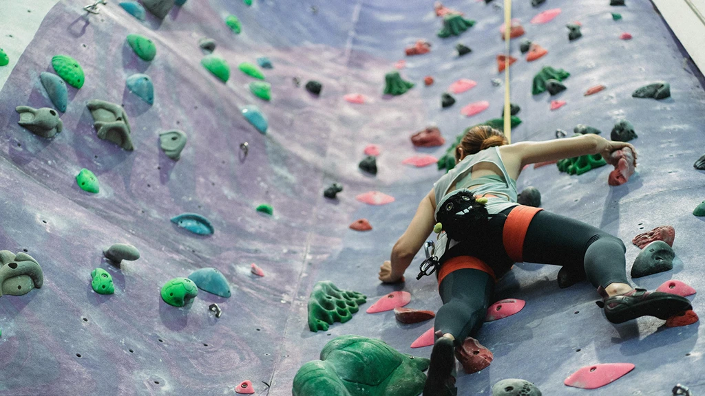 Klättrare på färgglad klättervägg med rosa och gröna grepp