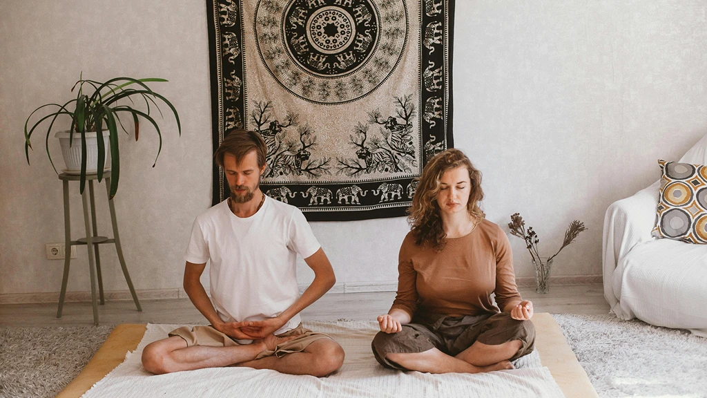 Par mediterar tillsammans i lotusposition på yogamatta i hemiljö