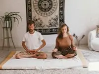 Par mediterar tillsammans i lotusposition på yogamatta i hemiljö