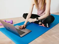 Kvinna följer onlineträning via dator på yogamatta hemma
